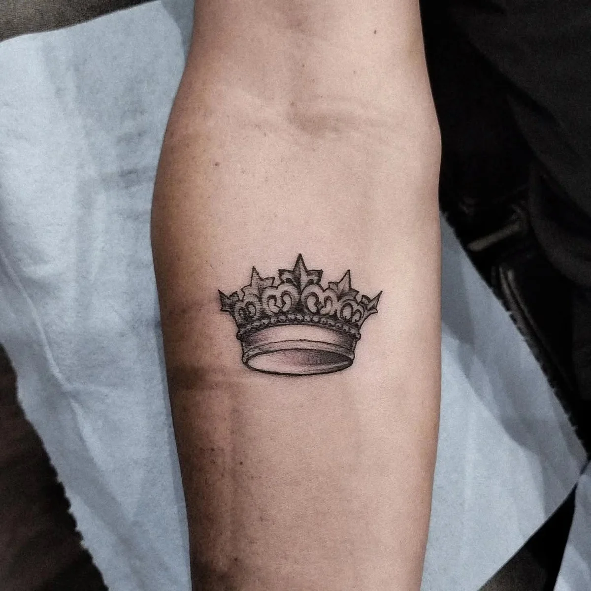 Corona — tatuaje pequeño de Kozo en antebrazo