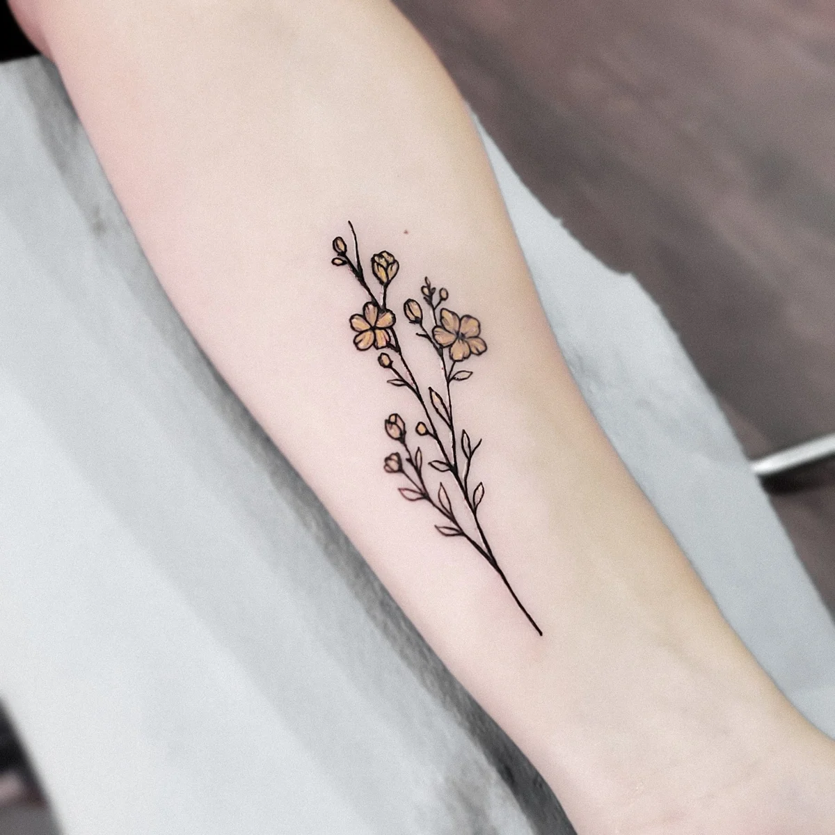 Ramita floral — tatuaje pequeño de Kozo en antebrazo